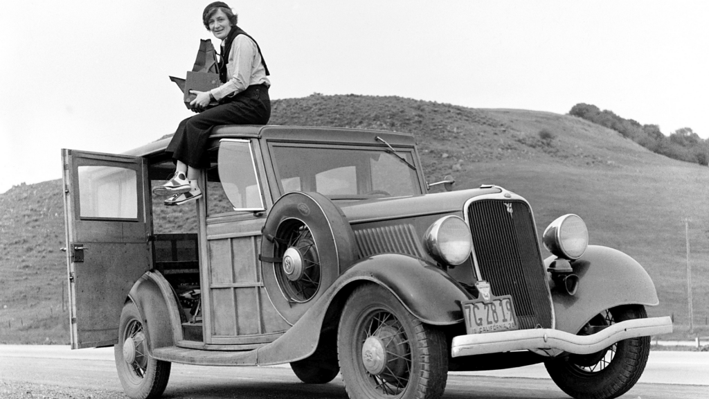 woman sat atop an old Ford in black and white with a hill in the background